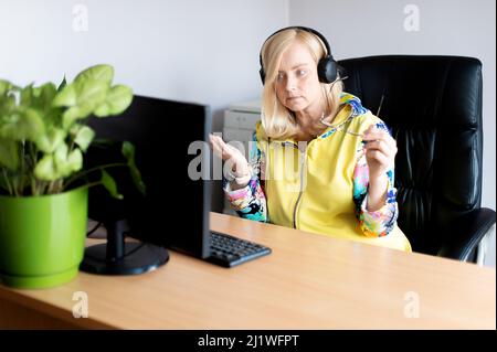 Ritratto di una donna di mezza età che indossa cuffie e guarda il webinar sul computer dell'ufficio Foto Stock