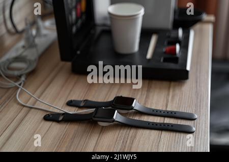 Due orologi di mele nere in carica, macchina da caffè con capsule su tavola di legno Foto Stock