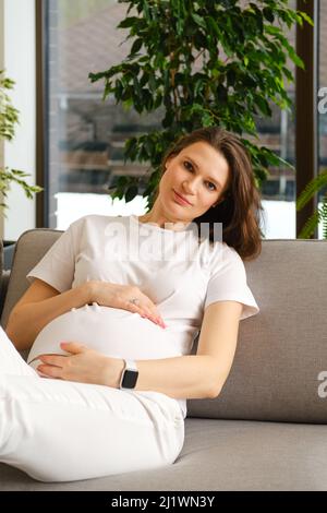 Bella donna incinta che riposa sul divano a casa Foto Stock