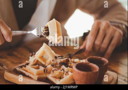 Cialde belghe con cioccolato, bacche e zucchero in polvere, una mano con un coltello e forchetta, bicchiere di caffè in corso di mangiare. Bruxelles bre Foto Stock