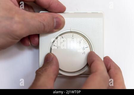 Una persona che abbassa il termostato della stanza di riscaldamento centrale per risparmiare sul costo di energia. Foto Stock