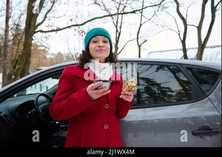 Fidata guida donna, viaggia in auto attraverso la natura innevata. Riposatevi in una pineta, uno spuntino sulla strada durante un viaggio nella stagione invernale. Enj Foto Stock