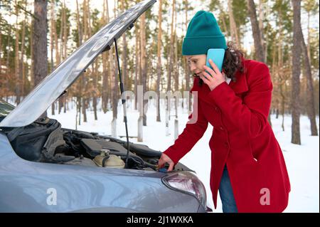 Stordito donna caucasica di mezza età cercando di riparare guasto auto o guasto motore e in attesa di servizio di traino per aiutare incidente auto sulla strada. Roa Foto Stock