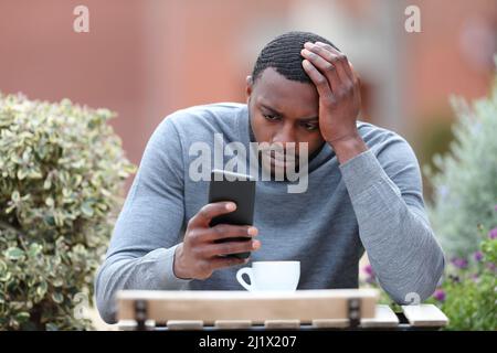 Vista frontale ritratto di un uomo preoccupato con pelle nera controllo telefono in una caffetteria