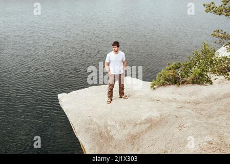 Il viaggiatore si erge su una roccia sopra l'acqua. L'uomo gode di una splendida vista sul mare. I pini crescono dalla pietra. Il concetto di vera avventura e silenzio. Foto Stock