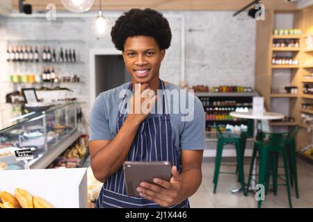 Ritratto di sicuro giovane barista afroamericano maschile con PC tablet sorridente al coffee shop. Inalterato, cultura caffè, persone e occupazione con Foto Stock