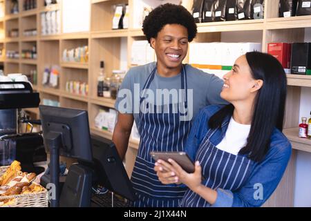 Allegri colleghi del coffee shop multirazziale che discutono con un tablet pc al banco del check-out. Inalterati, cultura del caffè, gente e occupazione concep Foto Stock