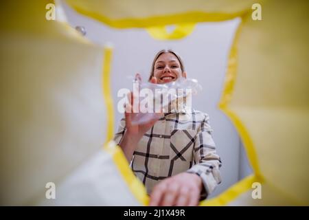 Immagine dall'interno del sacchetto giallo di riciclaggio della donna che lancia una bottiglia di plastica per riciclare. Foto Stock