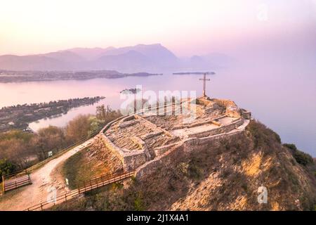 Veduta aerea della fortezza con una croce su una collina sullo sfondo del Lago di Garda. Panorama sulla rocca di manerba vista dall'alto. Foto Stock