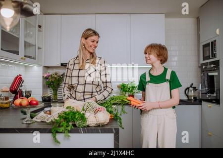 Madre disimballaggio cibo locale in confezione zero rifiuti da sacchetto con l'aiuto di figlia in cucina a casa. Foto Stock