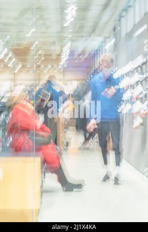 Giovane assistente alle vendite che aiuta la donna cliente a scegliere le scarpe sportive. Sfondo sfocato astratto del negozio di sport Foto Stock