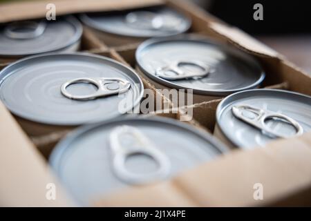 Lattine alimentari in una scatola di cartone aperta. Immagine concettuale per la rottura della catena di fornitura, la carenza di cibo, le scorte in tempi di guerra. Messa a fuoco selettiva. Foto Stock