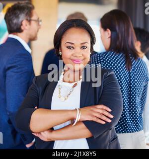 Im andare dopo il successo. Ritratto corto di una donna d'affari in piedi in ufficio con i suoi colleghi in background. Foto Stock