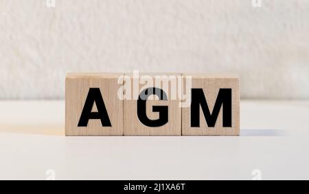Un blocco di legno con la parola AGM Assemblea generale annuale scritta su di esso su uno sfondo bianco. Foto Stock