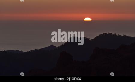 Tramonto con sole luminoso che scende sul mare all'orizzonte visto da Roque Nublo, Gran Canaria, Isole Canarie, Spagna con cielo colorato. Foto Stock