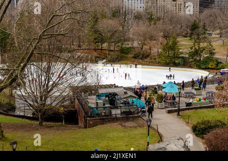 Wollman Rink con People Ice Skating durante il giorno d'inverno, vista dalla distanza, Central Park New York City, panchine e persone che camminano nel f Foto Stock