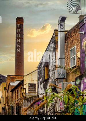 Il camino della Birreria di Truman si vede contro un cielo dorato, con edifici fortemente graffiti in primo piano. Londra. REGNO UNITO Foto Stock