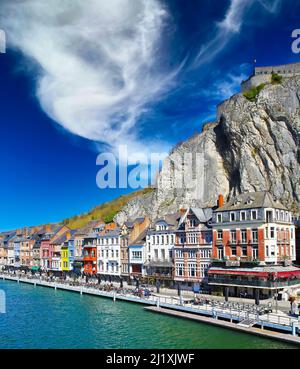 Dinant, Belgio - Marzo 9. 2022: Vista sul lungofiume case colorate contro ripide pareti rocciose, cielo blu impressionsiv Foto Stock