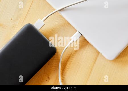 Power Bank carica un computer portatile tramite cavo USB di tipo C su sfondo in legno Foto Stock
