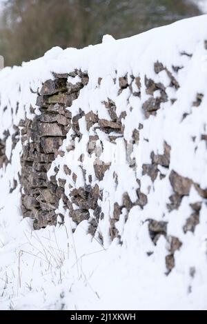 Un muro di pietra cotswold attraverso un campo di framer coperto da una leggera caduta di neve. Foto Stock