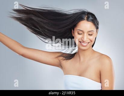 I miei capelli sono perfetti. Scatto di una giovane donna attraente in piedi da sola nello studio e flipping i suoi capelli. Foto Stock