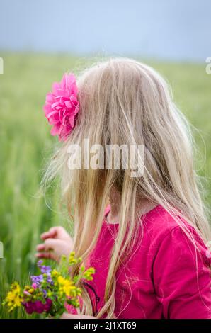 ragazza con capelli biondi lunghi vista posteriore e fiori colorati in mano Foto Stock