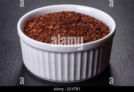 Tè Rooibos in una ciotola bianca su sfondo nero. Disposizione piatta, vista dall'alto, spazio di copia Foto Stock