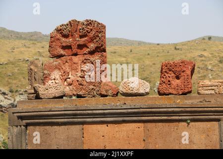 Un primo piano di khachkars su una piattaforma di pietra arancione con montagne e colline sullo sfondo Foto Stock