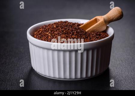 Tè Rooibos in una ciotola bianca su sfondo nero. Disposizione piatta, vista dall'alto, spazio di copia Foto Stock