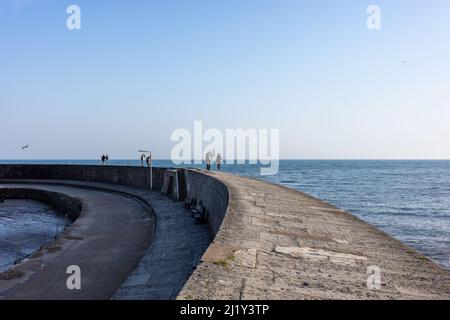 Persone che camminano lungo il muro del porto a Lyme Regis, Regno Unito (Mar22) Foto Stock