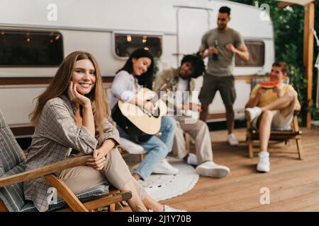 Giovani freschi divertirsi in campeggio, sedersi in sdraio, suonare la chitarra, bere birra, mangiare il cocomero Foto Stock