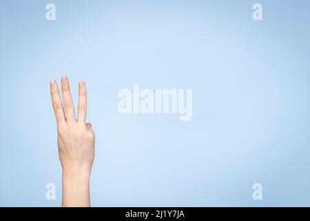 La mano femmina mostra il numero tre. Mano donna che mostra tre dita, puntando le dita su sfondo azzurro Foto Stock
