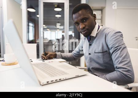 Un uomo d'affari nero afroamericano in una tuta etnica nazionale lavora a un computer portatile. Analisi e lavoro online Foto Stock