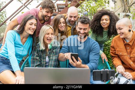 gruppo di persone diverse che creano contenuti on line guardando le statistiche direttamente dall'app per smartphone, giovani amici felici condividere su plat streaming Foto Stock