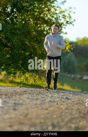 L'uomo che fa jogging nella natura rurale durante la splendida giornata estiva. Sport fitness modello caucasico etnia formazione all'aperto. Foto Stock