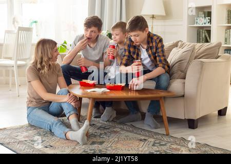 Una donna e tre ragazzi adolescenti, mangiando fast food in scatole rosse e bevendo bevande in lattine rosse. Foto Stock