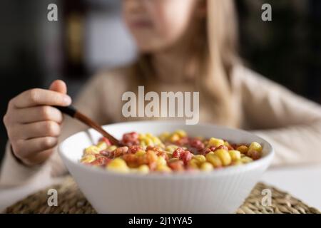 Carina ragazza caucasica seduta al tavolo in cucina mattina presto e la preparazione della colazione con cornflakes colorati e latte. Bambini che godono la vita con Foto Stock