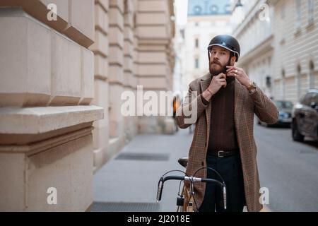 L'uomo bello mette sul casco prima di andare in bicicletta. Sicurezza e trasporto ecologico Foto Stock