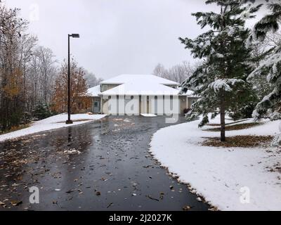 Strada asfaltata che porta ad una casa gemella o duplex ha molte foglie bagnate su di esso, a seguito di una recente caduta di neve, in un overcast giorno d'autunno in Minnesota. Foto Stock