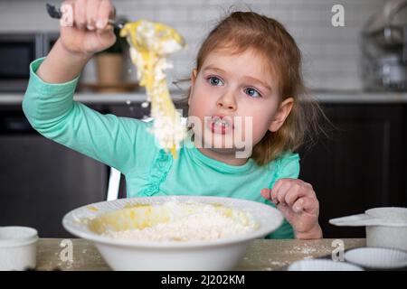 Piccolo bambino felice che cucinano in cucina. Piccola bella ragazza che fa pasta per pasticceria a casa. Carino bambino imparando a cuocere. Foto Stock