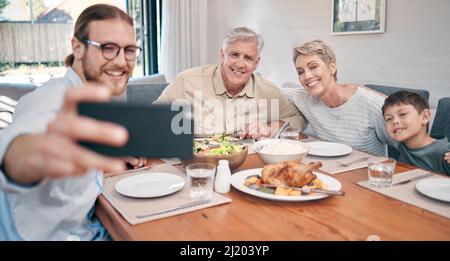 I ricordi più grandi di Lifes sono fatti fra il cibo e la famiglia. Shot di una famiglia che prende selfie mentre si fa un pasto insieme a casa. Foto Stock