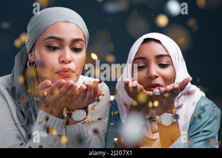 Lascia un po' di scintilla ovunque tu vada. Scatto corto di due donne giovani attraenti che indossano i hijab ed i confetti soffianti mentre si levano in piedi contro un Foto Stock