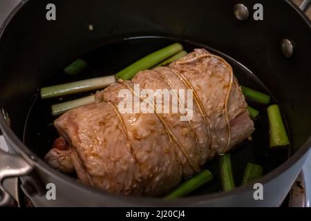 Primo piano, focalizzazione selettiva su una succosa cottura al forno a chashu di maiale in una pentola grande piena di salsa di soia e cipolle verdi Foto Stock