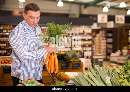 Uomo che sceglie la carota in supermercato Foto Stock