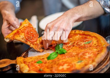 Foto ravvicinata delle mani di mans che prendono una fetta di pizza Foto Stock
