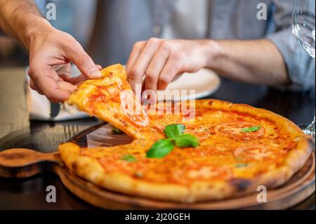 Foto ravvicinata delle mani di mans che prendono una fetta di pizza Foto Stock