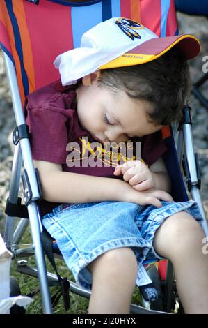 Bambino ragazzo, toddler, che dorme in stroller al gioco della sfera con i genitori con il logo Redskins sul cappello con il suo volto Foto Stock