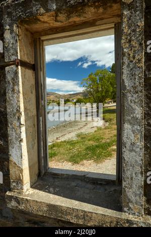 Guardando attraverso la finestra di edificio abbandonato al Lago Dunstan e Old Cromwell Town, Cromwell, Central Otago, South Island, Nuova Zelanda Foto Stock