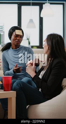 I colleghi che giocano a charades gioco con note adesive dopo il lavoro in ufficio. I compagni di lavoro si divertiranno a indovinare il gioco per fare attività e divertimento mentre bevono birra e mangiano pizza. Foto Stock