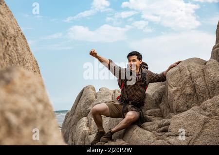 Zaino in spalla giovane con braccia distese sulle rocce della spiaggia - foto di scorta Foto Stock